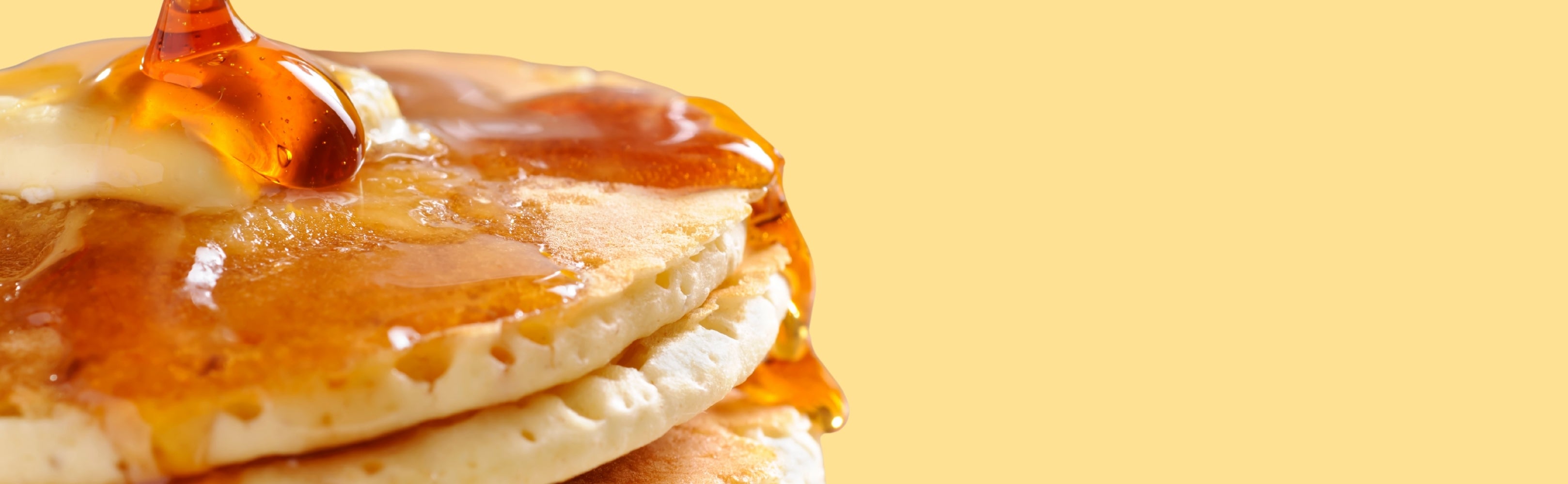 Stack of pancakes with syrup on a yellow background