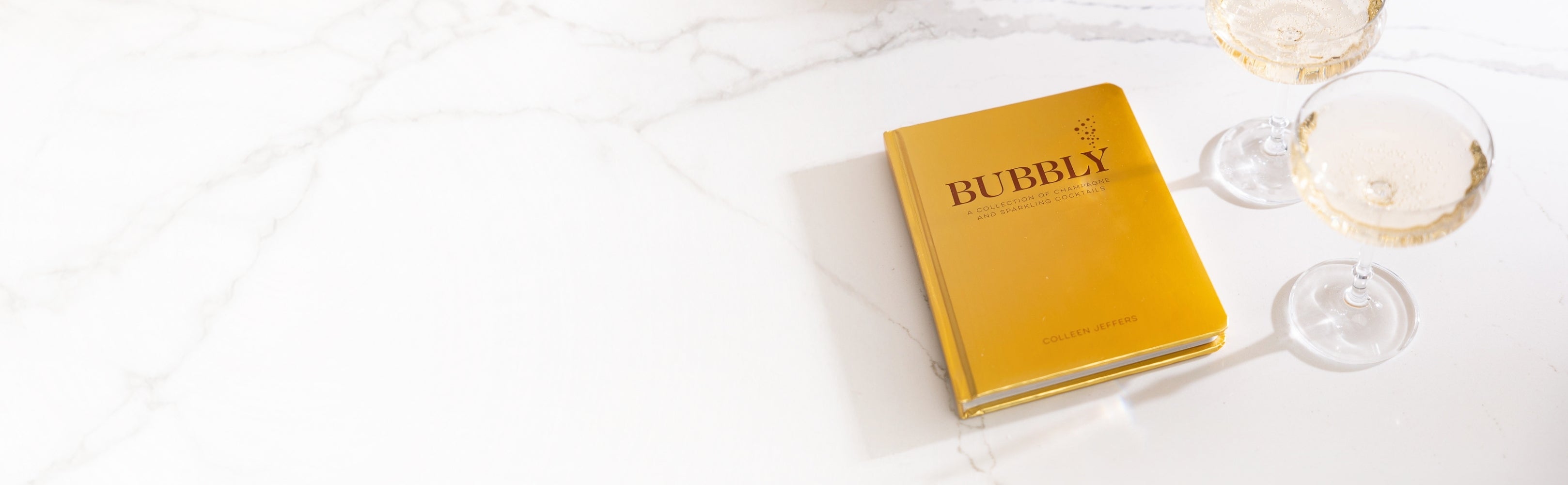 Yellow book titled 'Bubbly' on a white surface with two wine glasses.